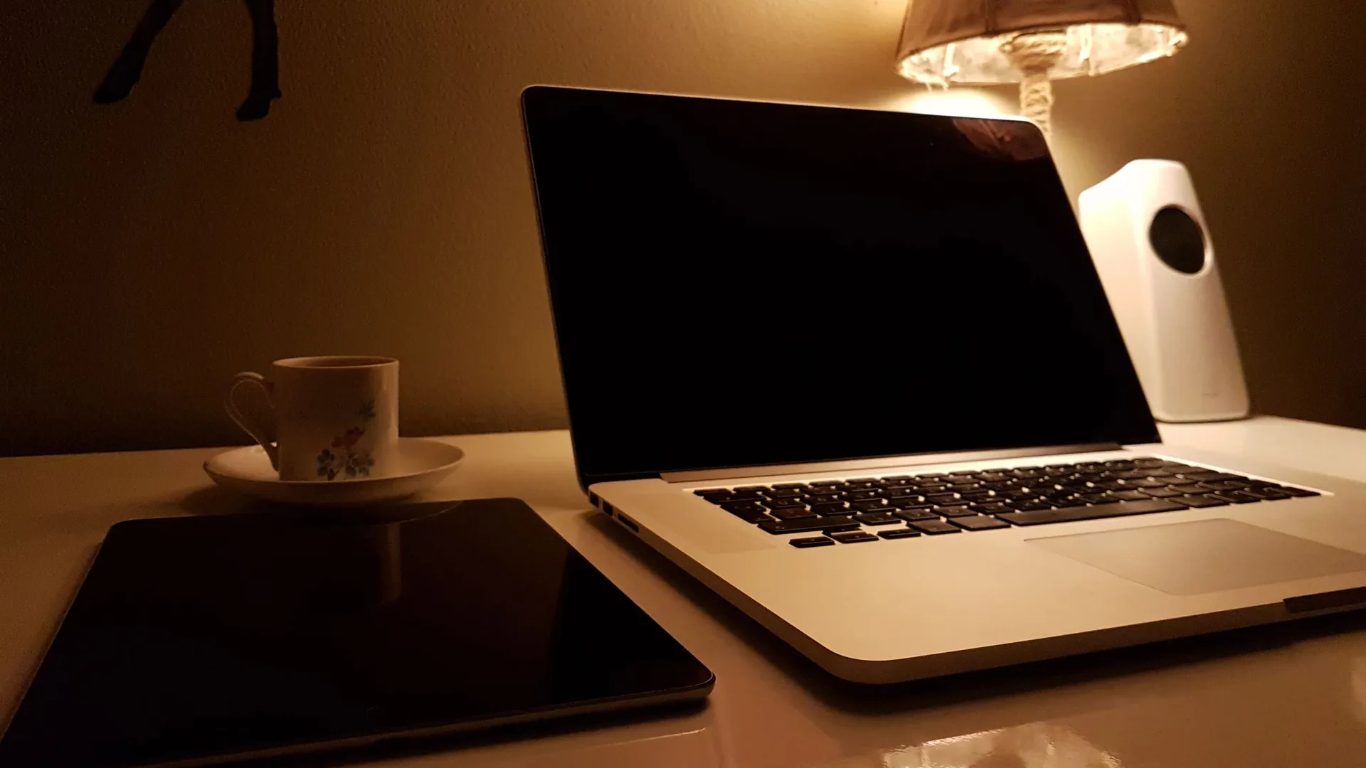Notebook com a tela apagada sobre uma mesa iluminada por um abajur, num ambiente aconchegante