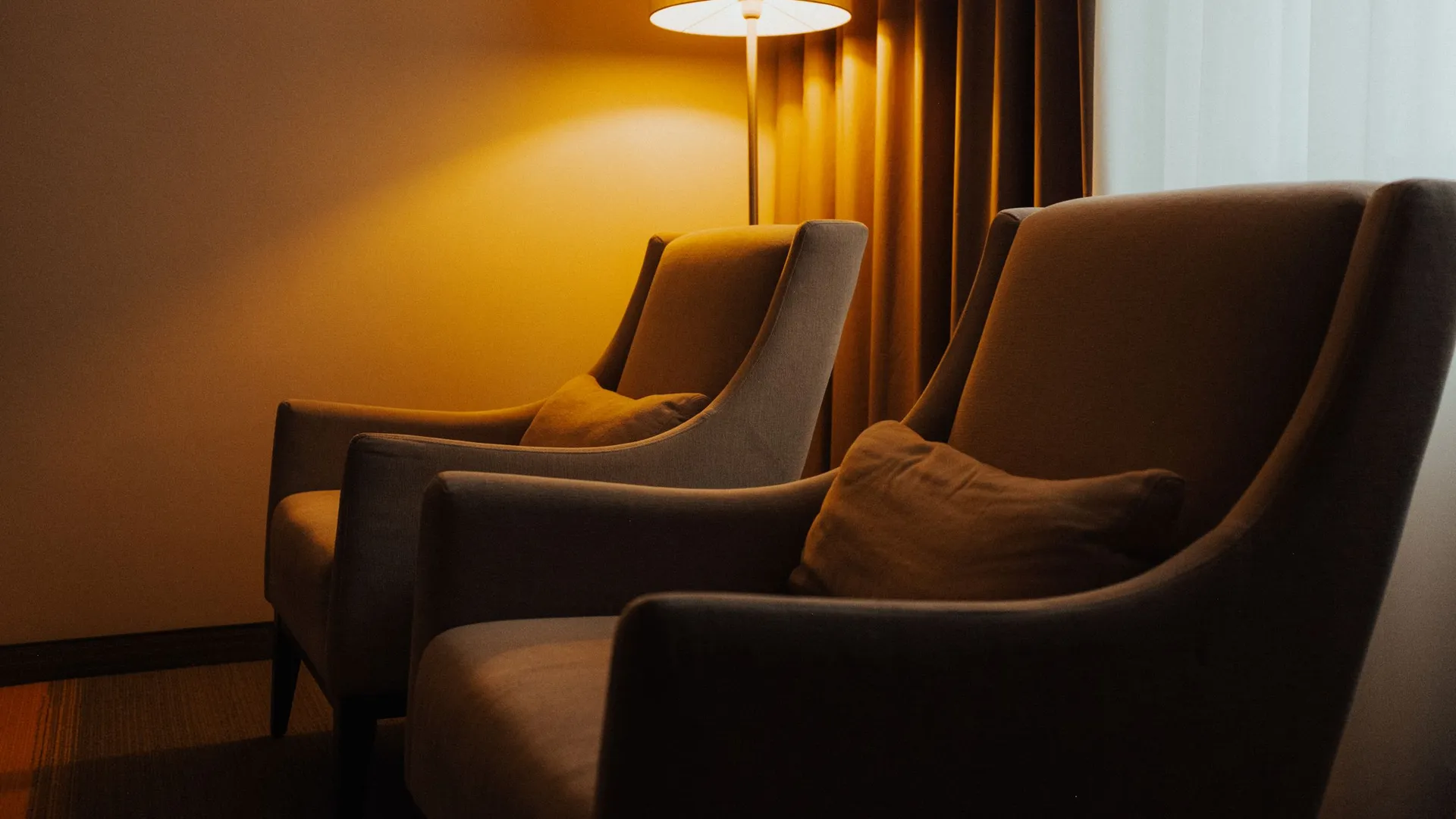 Duas poltronas e um abajur aceso numa sala de atendimento com luz quente